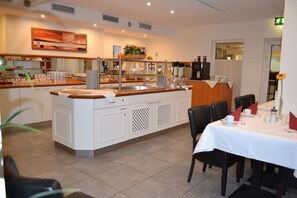 A restaurant with a central island counter, white cabinetry, and a dining area with tables set for service. - Best Western Hotel Erlangen (Erlangen)