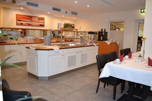 Restaurante com balcão central em ilha, armários brancos e área de refeições com mesas preparadas para o serviço.