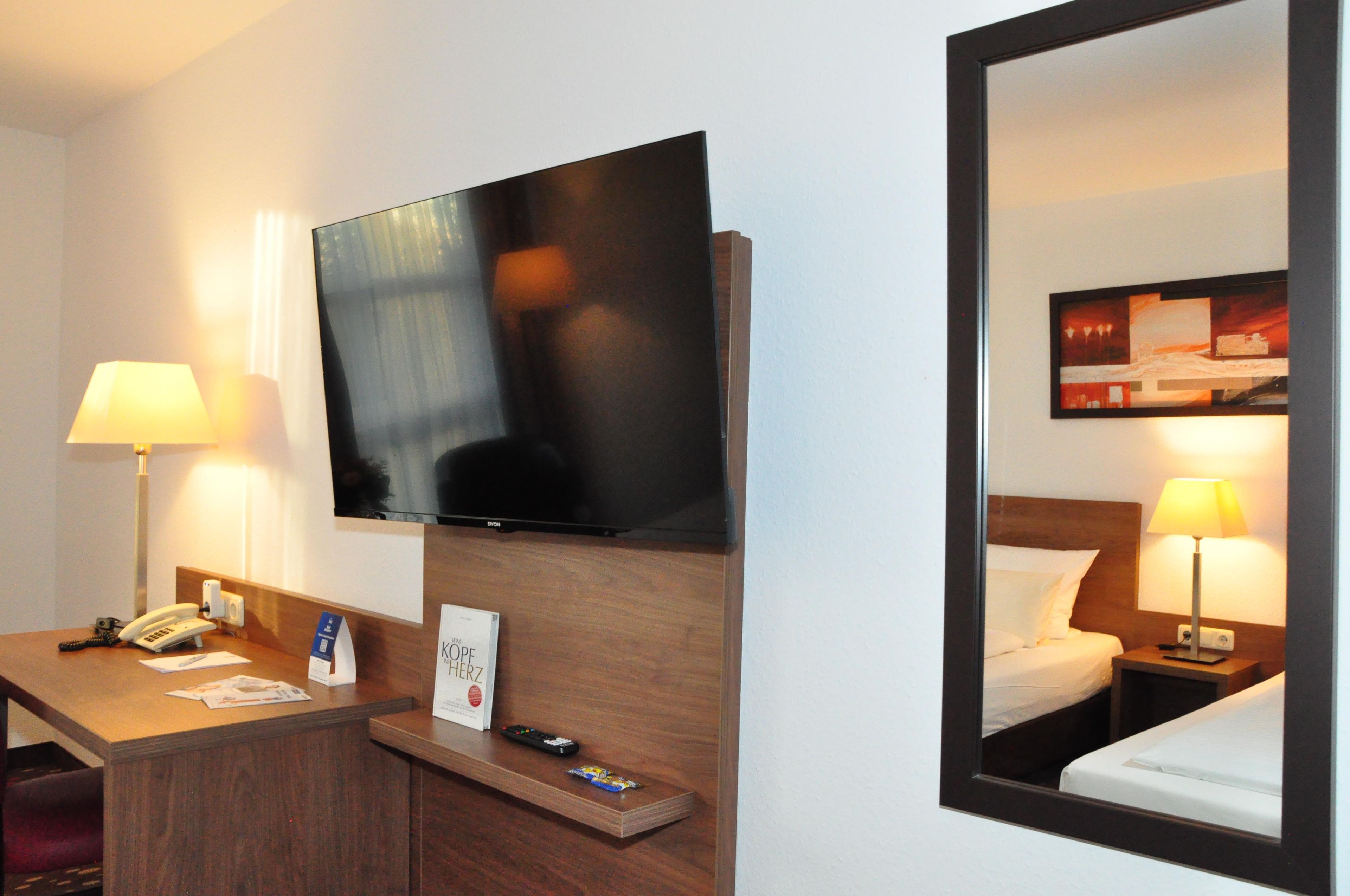 Une chambre d’hôtel équipée d’un téléviseur à écran plat fixé au mur, d’un bureau avec un téléphone, une télécommande et un petit porte-cartes.