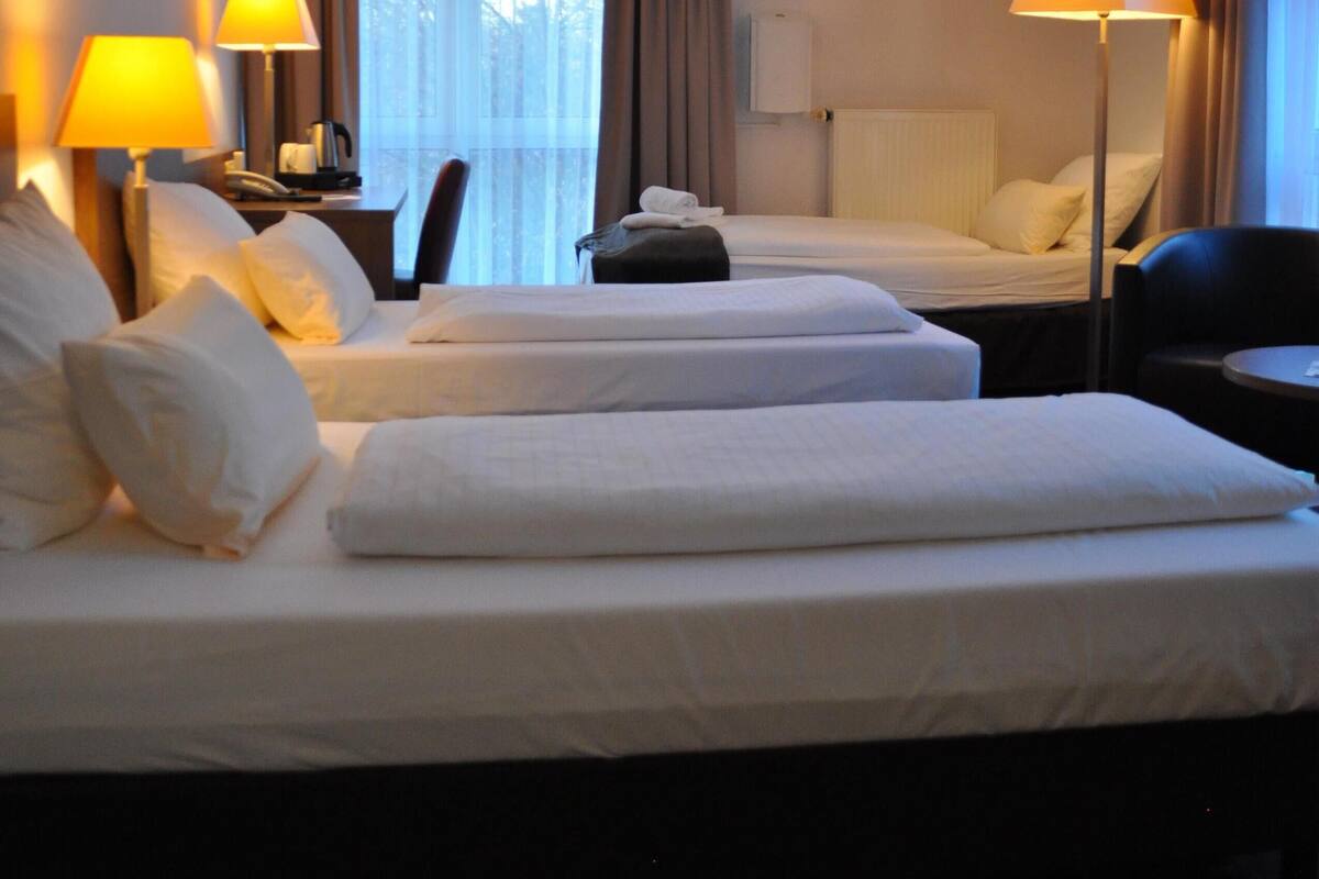 A hotel room with two beds, a desk, a chair, and two lamps.