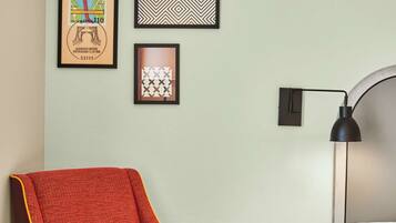 Une chambre d’hôtel avec un fauteuil rouge, une petite table en bois, un lit et une lampe fixée au mur.
