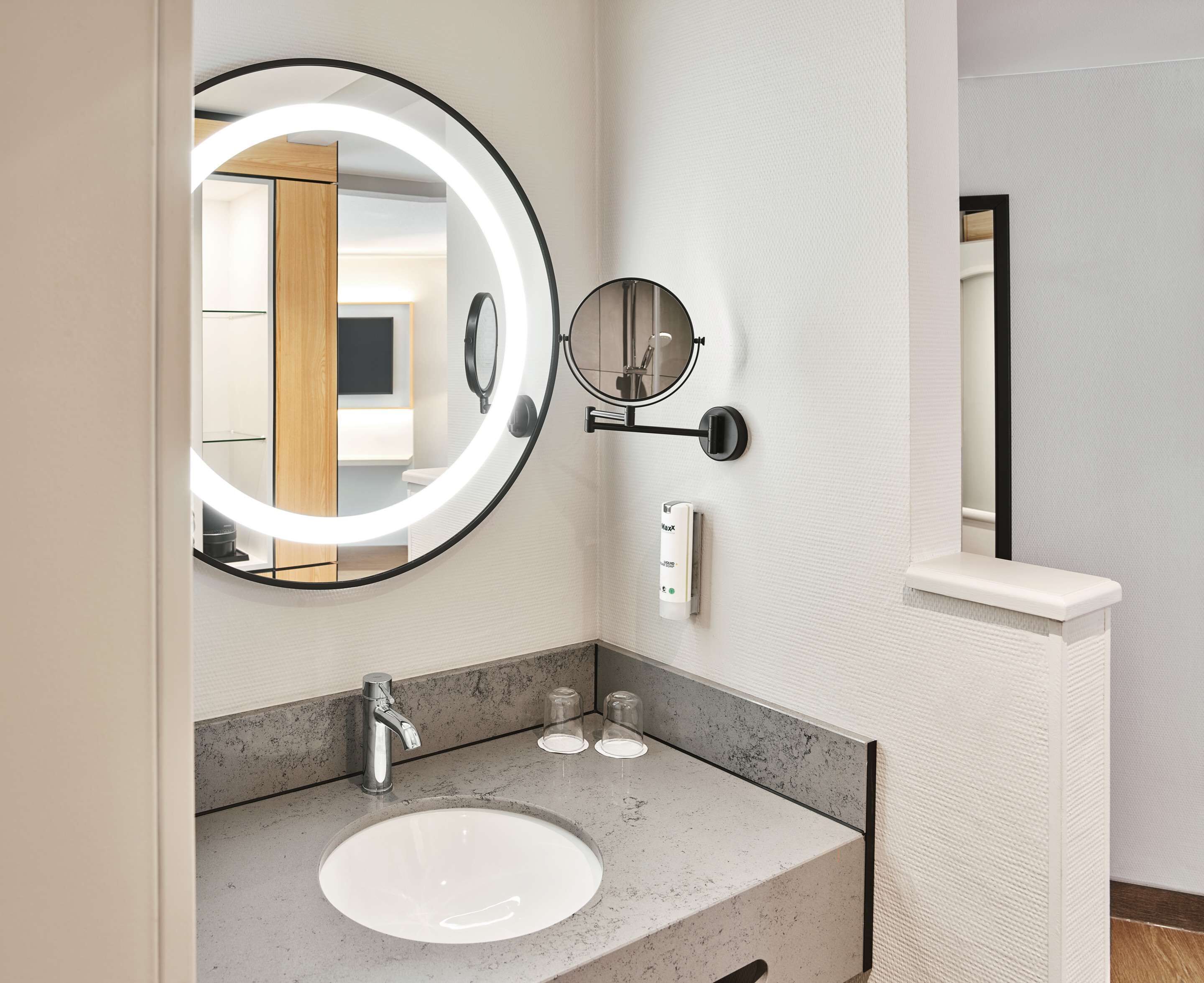 A modern bathroom with a round mirror, a sink, and a towel rack.