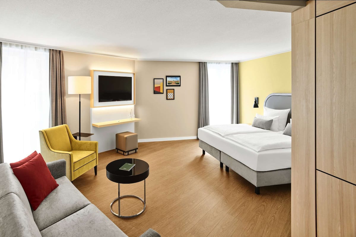 Ein modernes Hotelzimmer mit einer Couch, einem gelben Sessel, einem Bett, einem Fernseher und einem kleinen Tisch.