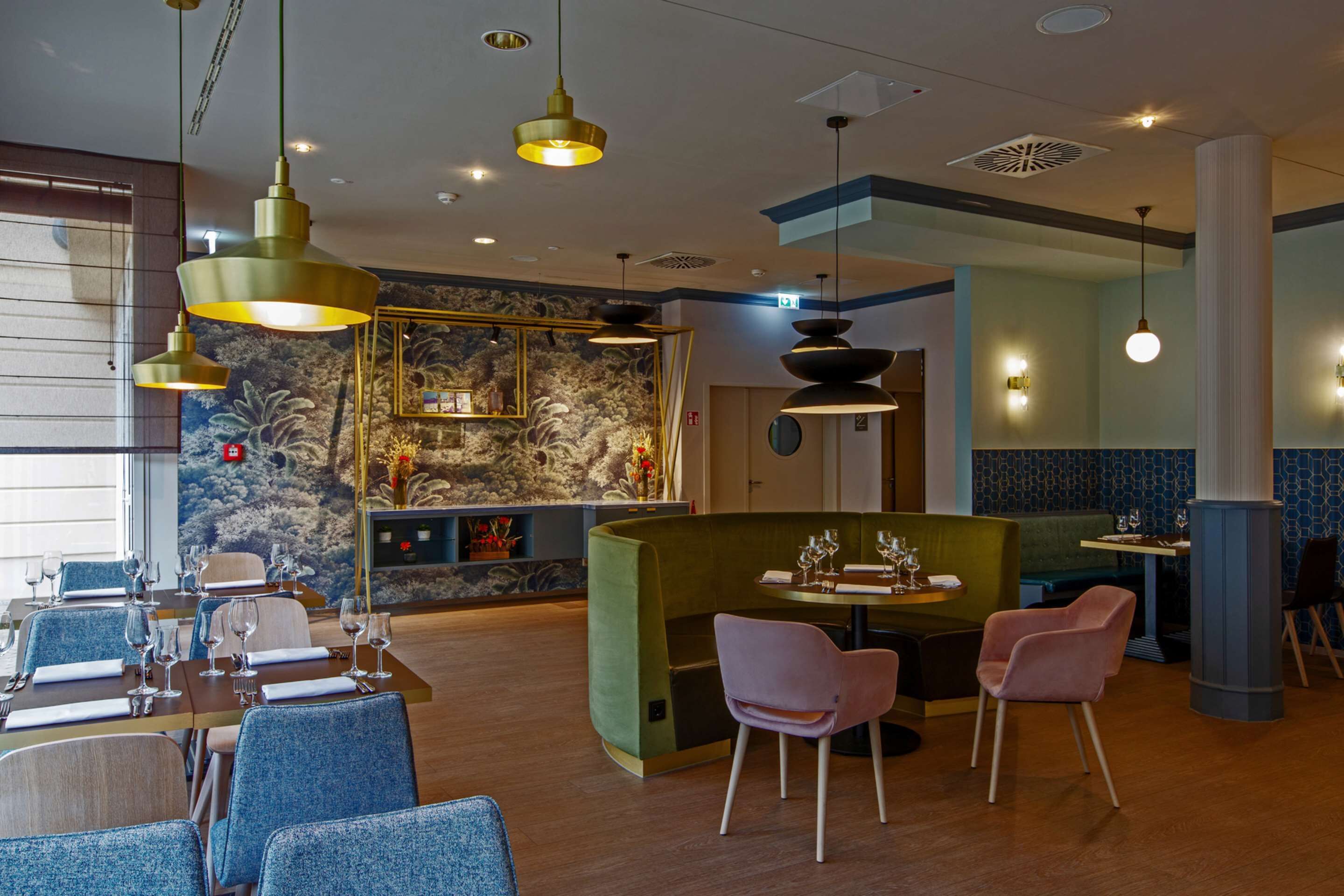 Ein Restaurant mit blauen Polstersesseln, einer grünen Essecke und Pendelleuchten.