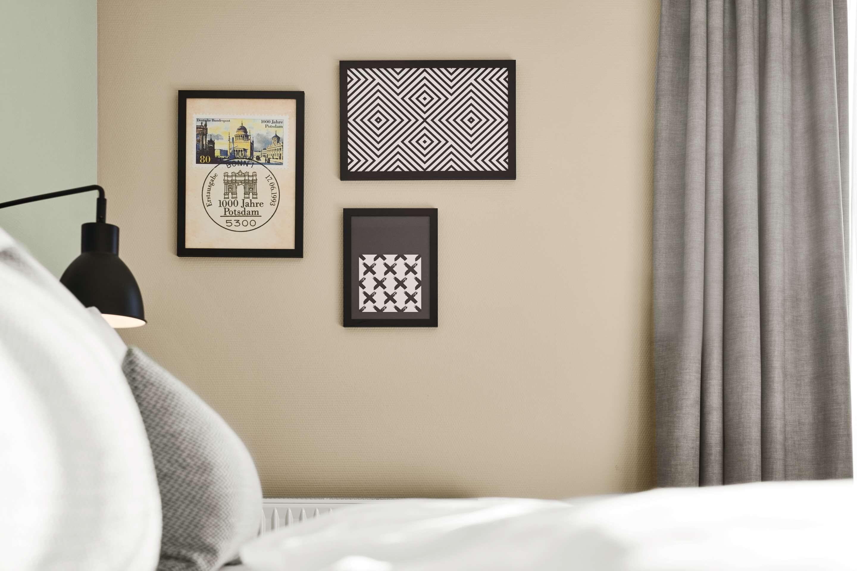 A bedroom with a bed, a lamp, and three framed pictures on the wall.