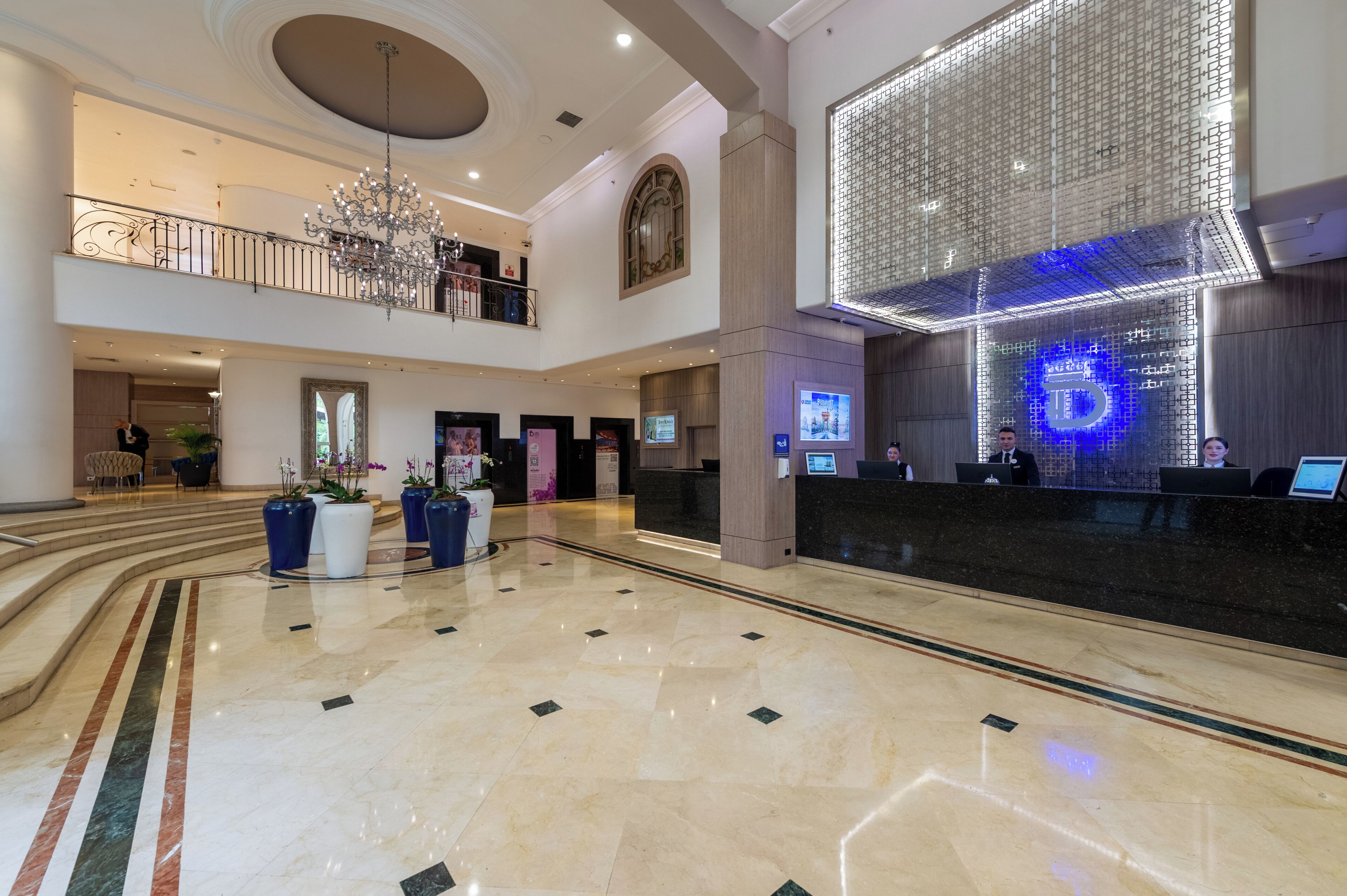 A spacious lobby with a reception desk, a chandelier, and a high ceiling.