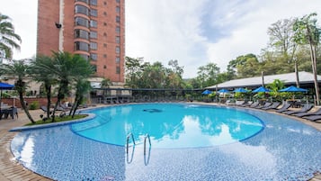 Una piscina con bordo piastrellato, circondata da lettini e ombrelloni, con un edificio alto sullo sfondo.