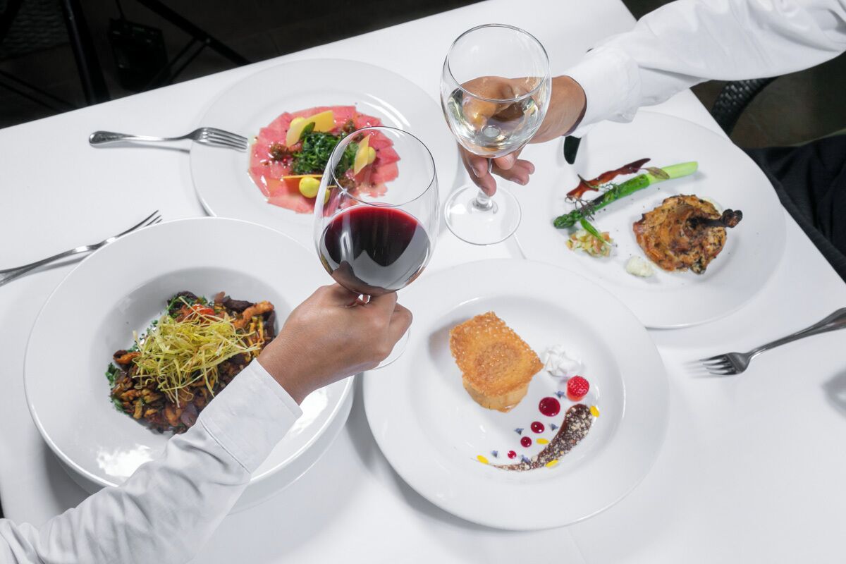 A dining table with plates of food and a glass of red wine.
