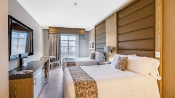 A hotel room with two beds, a desk, a TV, and a window with curtains.