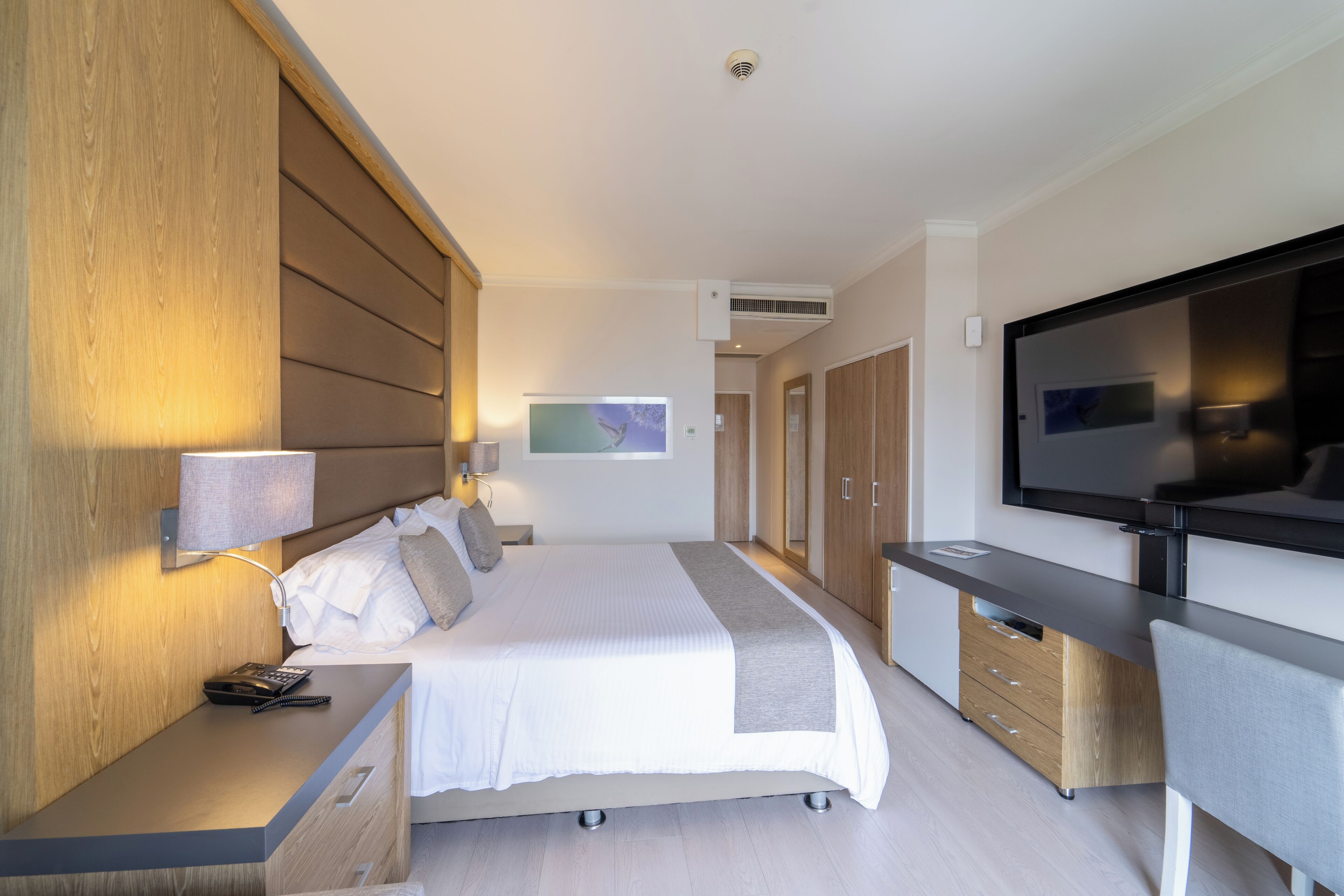 A modern hotel room with a bed, bedside table, lamp, TV, and wardrobe.