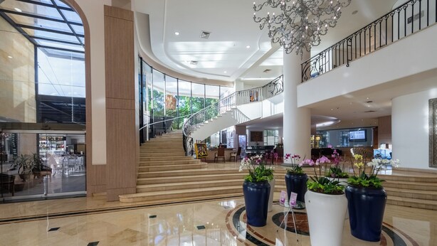 A spacious lobby with a central staircase, large potted plants, and a chandelier.