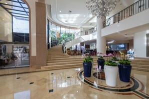 A spacious lobby with a central staircase, large potted plants, and a chandelier.
