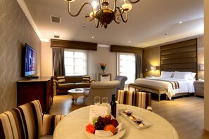 A hotel room with a bed, a sofa, a dining table with fruit and a bottle, and a TV on a stand. - Dann Carlton Medellin Hotel (Medellín)