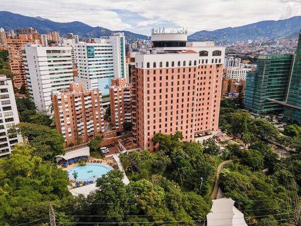 A high-rise building with a swimming pool, surrounded by greenery and other buildings. - Dann Carlton Medellin Hotel (Medellín)