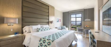 Habitación de hotel moderna con una cama grande, mesitas de noche, un escritorio y vistas a la ciudad.