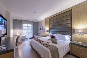 A hotel room with a bed, bedside table, TV, desk, and seating area. - Dann Carlton Medellin Hotel (Medellín)