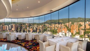A restaurant with a panoramic city view, high ceilings, and modern furnishings.