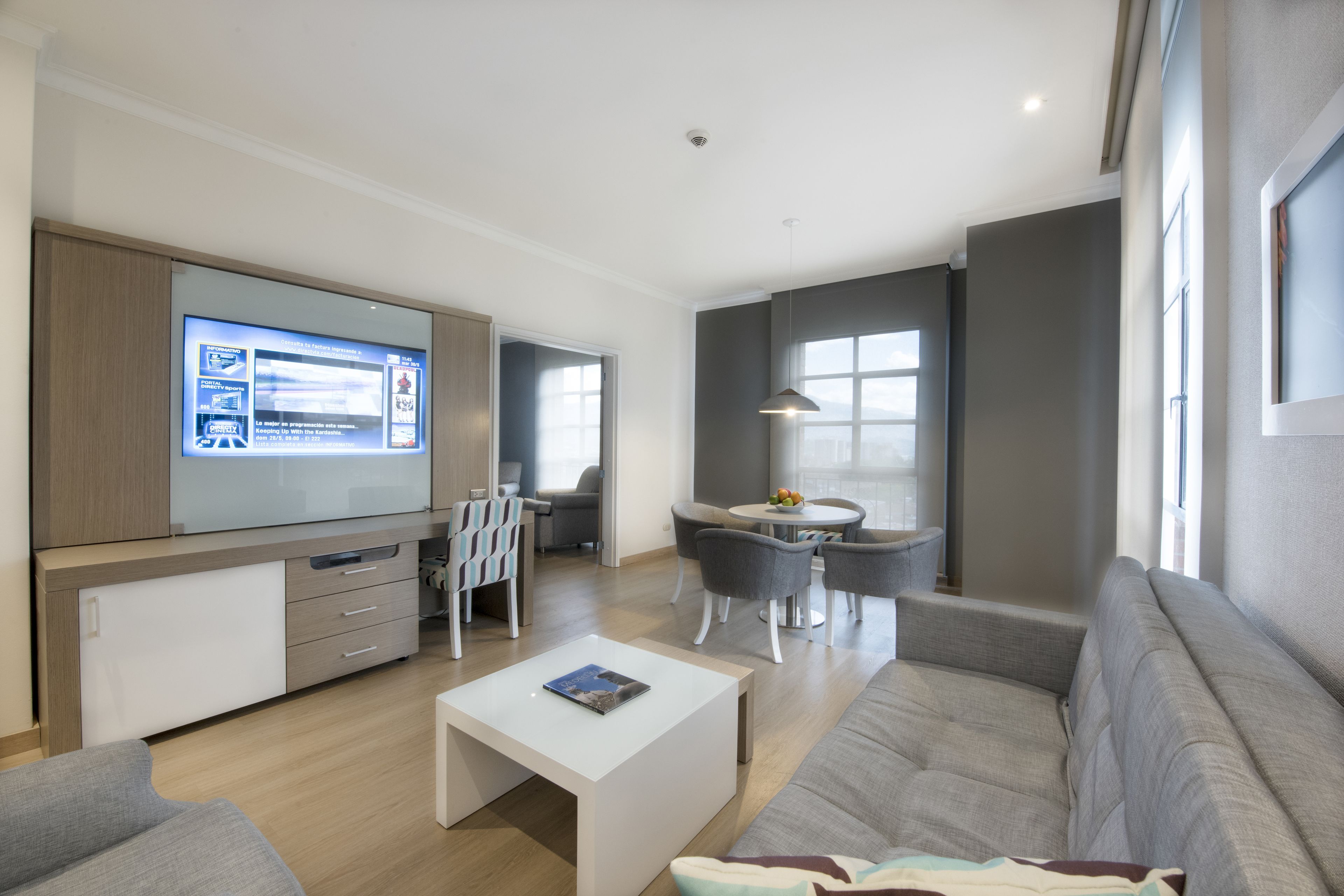 Una sala moderna con televisor de pantalla plana, un sofá, una mesa de centro y un comedor con sillas y una mesa.