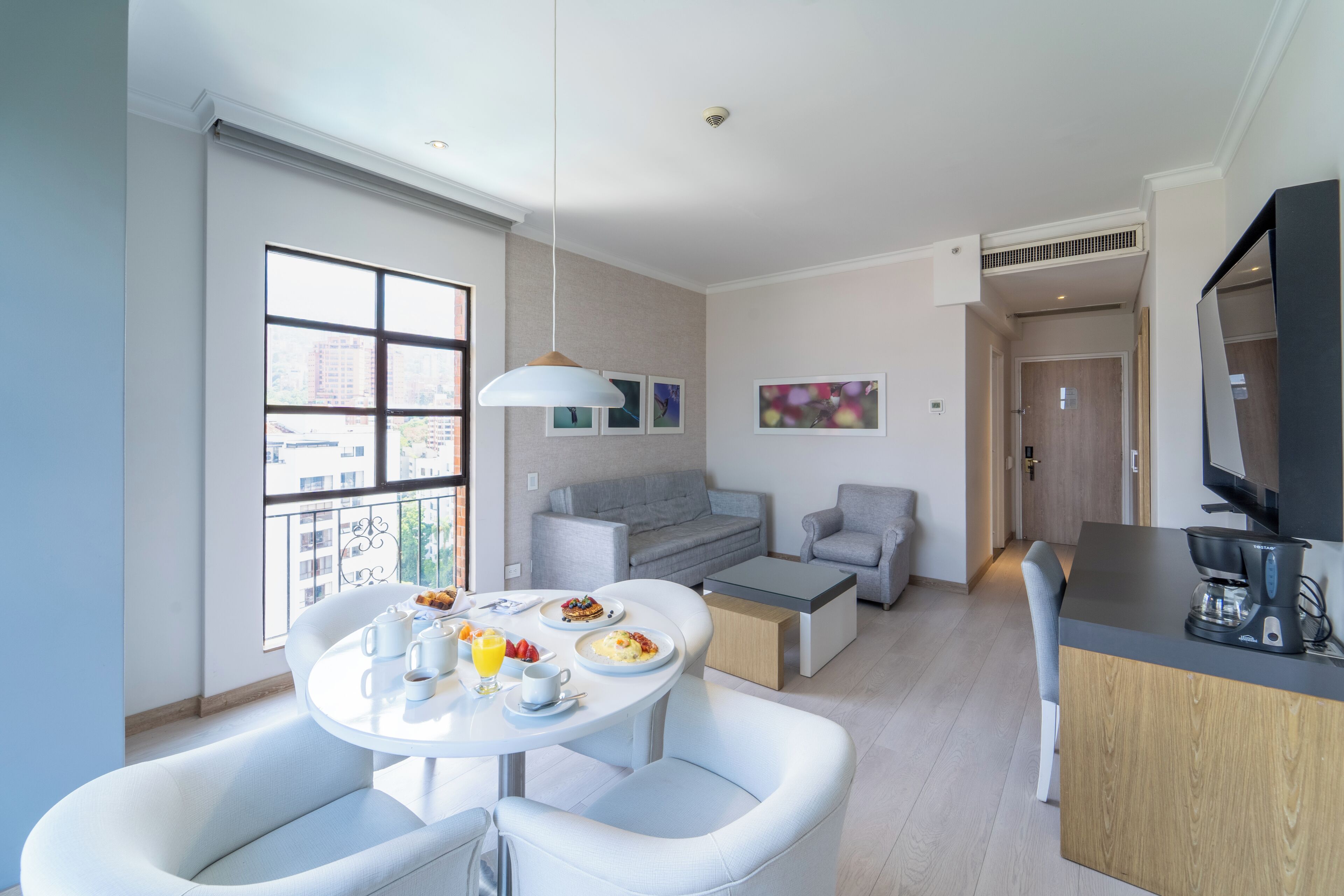 Un salon moderne comprenant un coin repas, des canapés gris, une table basse et un téléviseur.