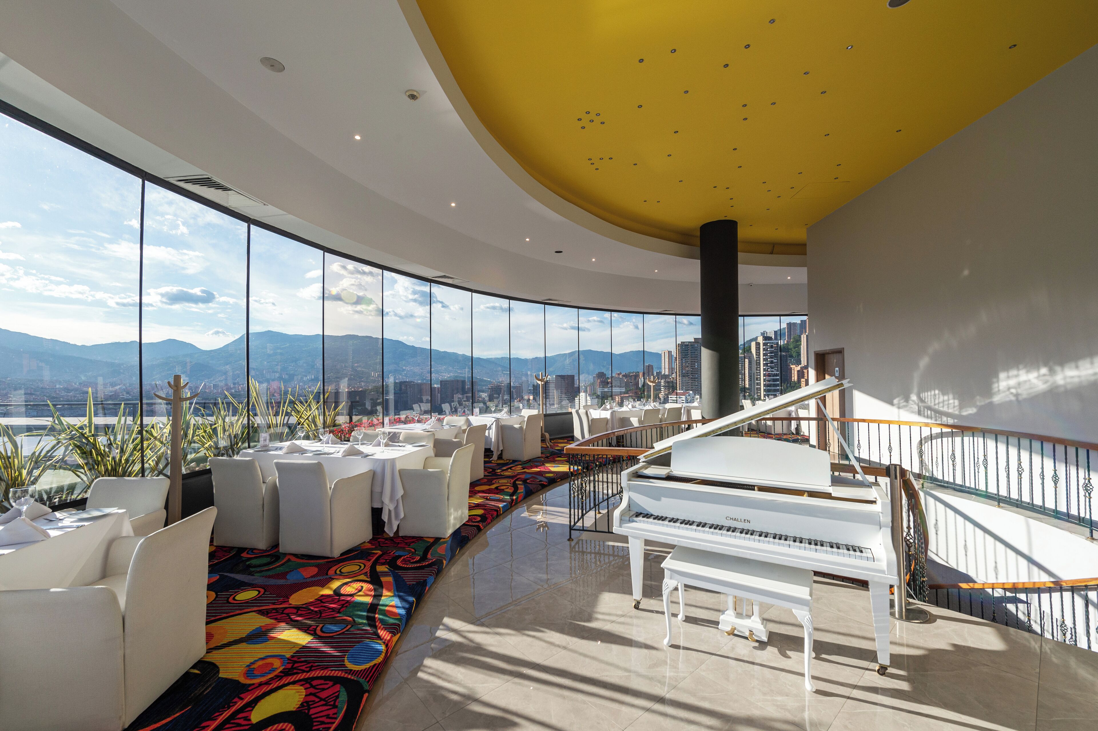 A modern lounge area with a grand piano, white furniture, and a colorful carpet.