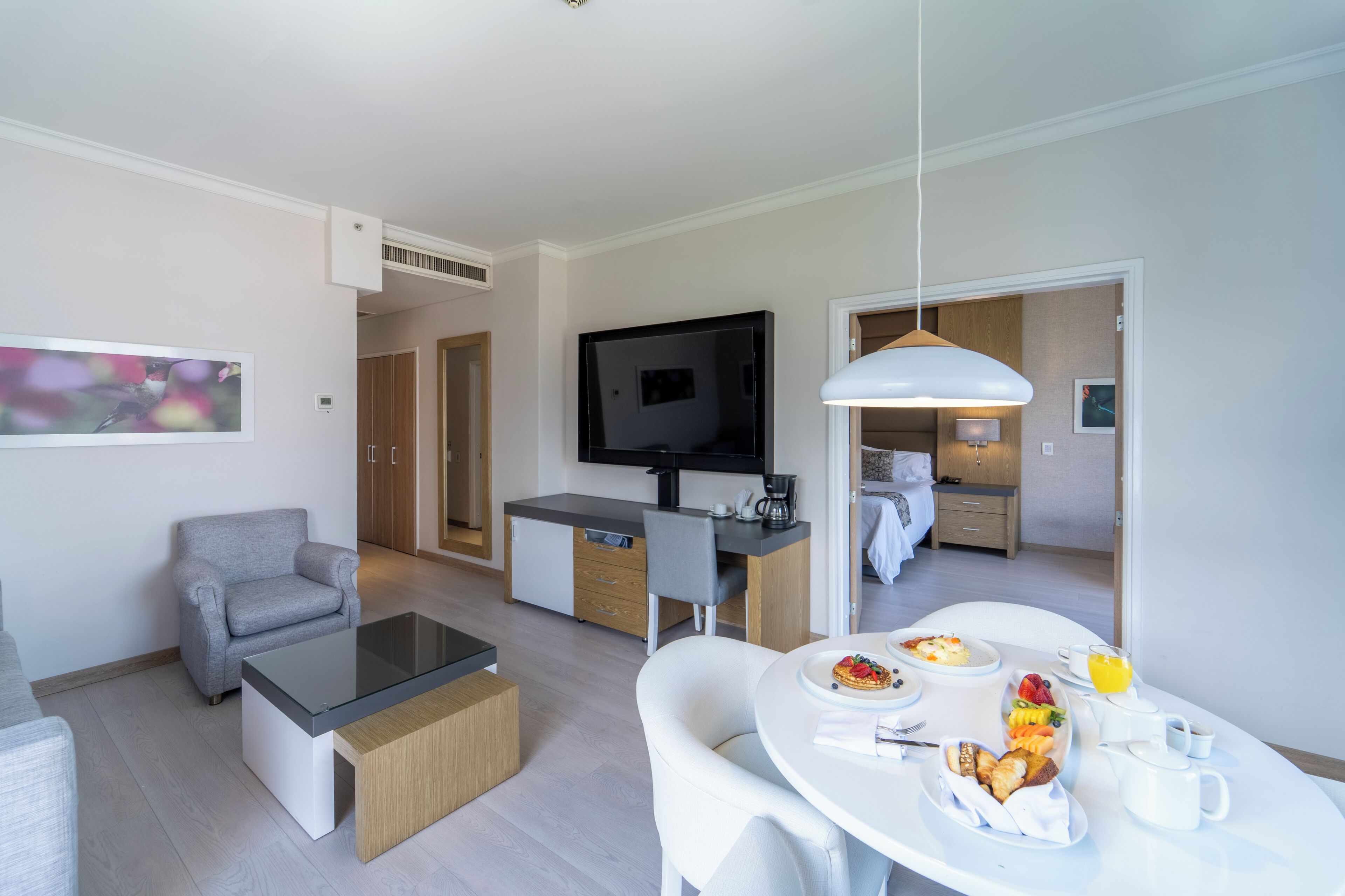 Una sala de estar moderna con sofá, mesa de centro, televisor y un comedor con desayuno.