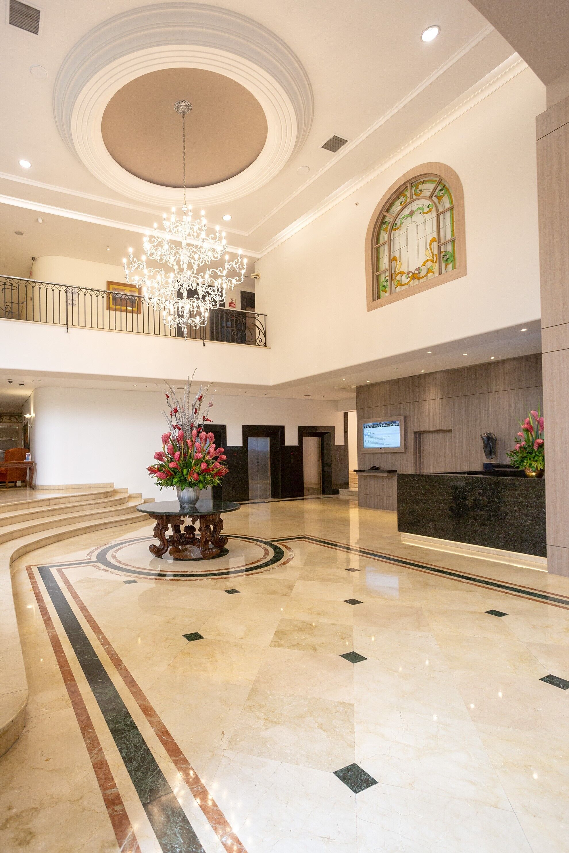 Un'ampia hall con un imponente lampadario, una reception e un'ampia finestra a vetri colorati.