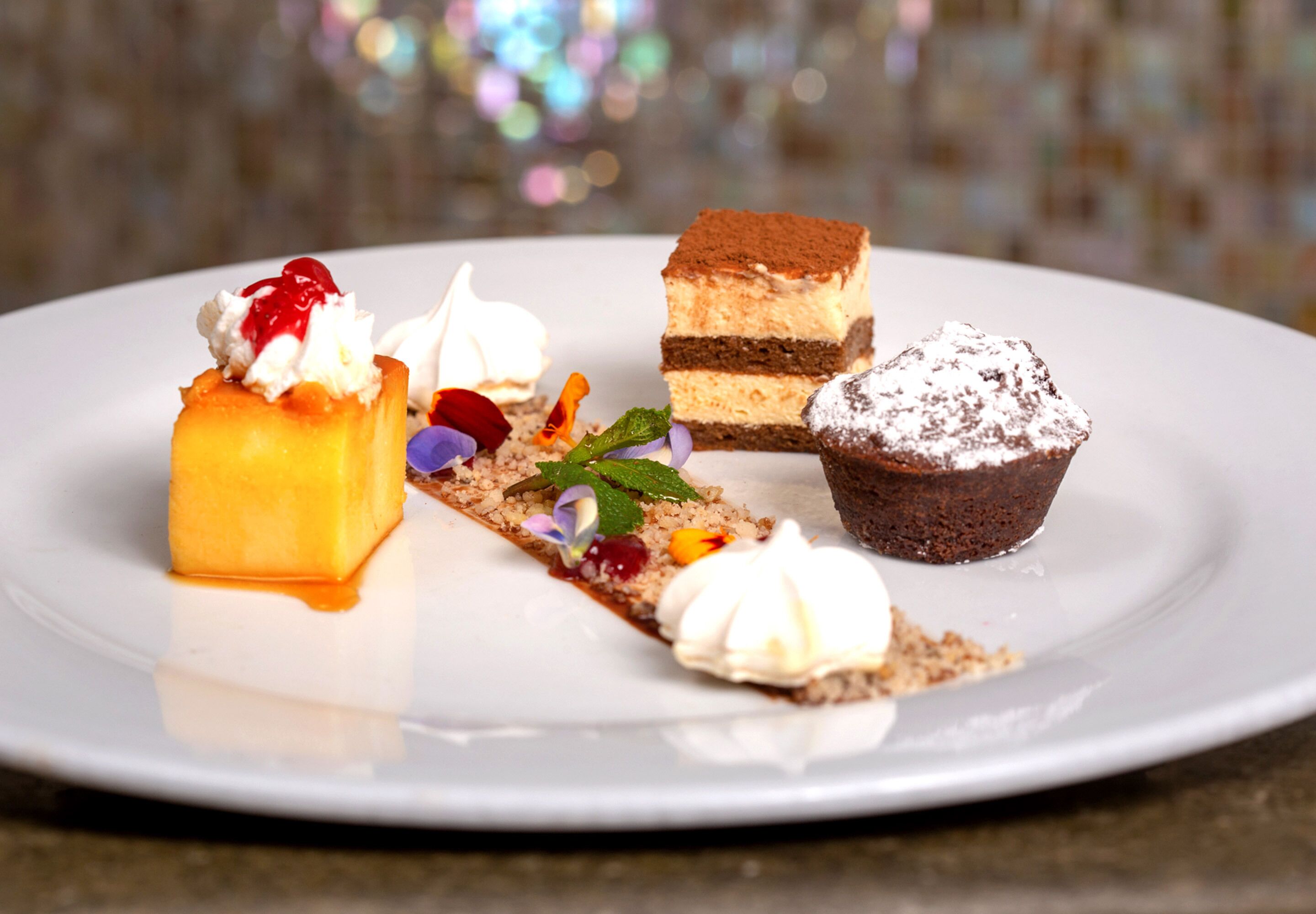 Ein Dessertteller mit verschiedenen süßen Köstlichkeiten, darunter ein Stück Schichttorte, ein Cupcake und ein quadratisches Dessert mit Schlagsahne.
