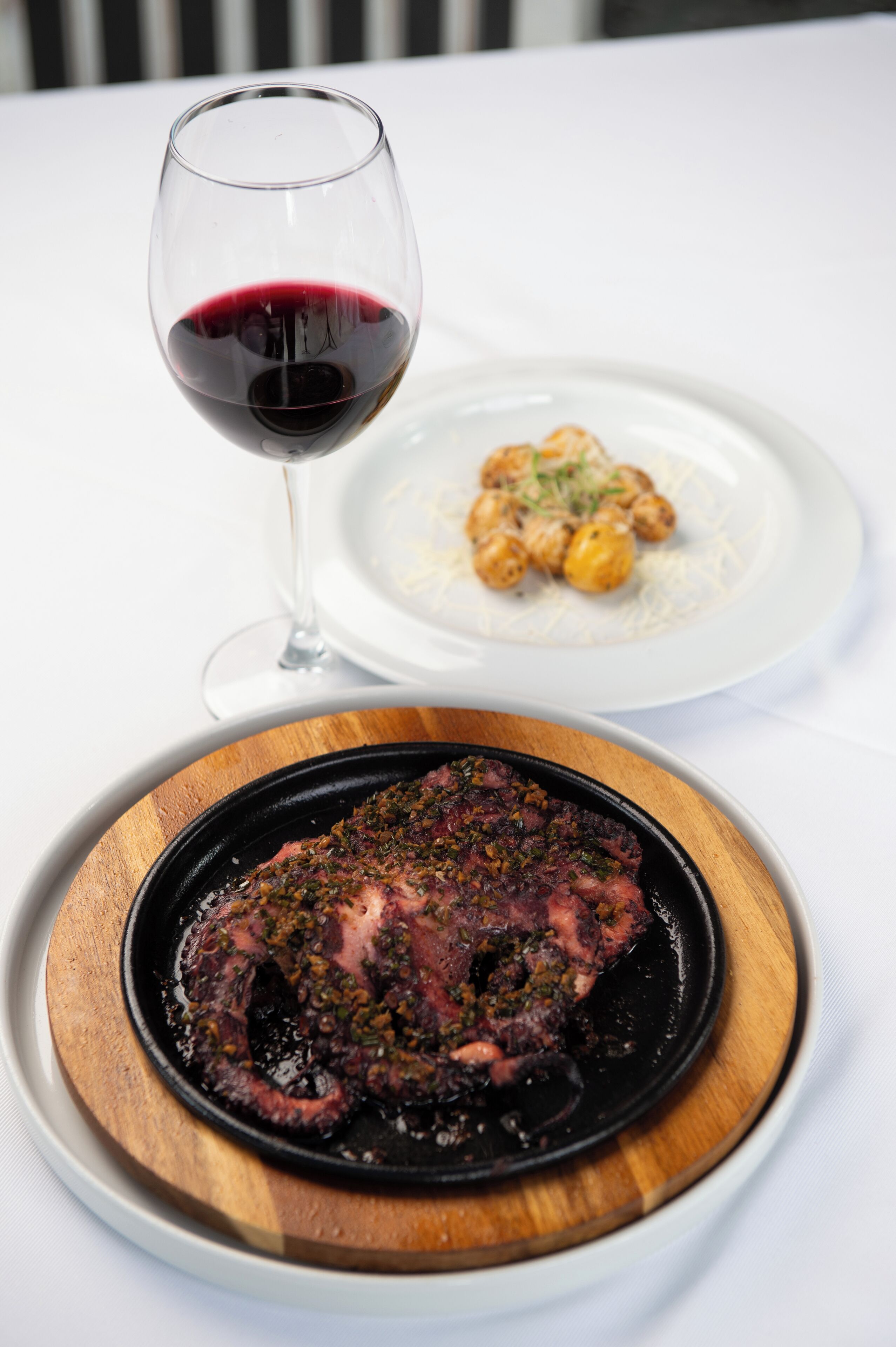 A dining table with a plate of octopus and a glass of red wine.