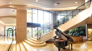 A grand lobby with a grand piano, a staircase, and a large window overlooking a garden.
