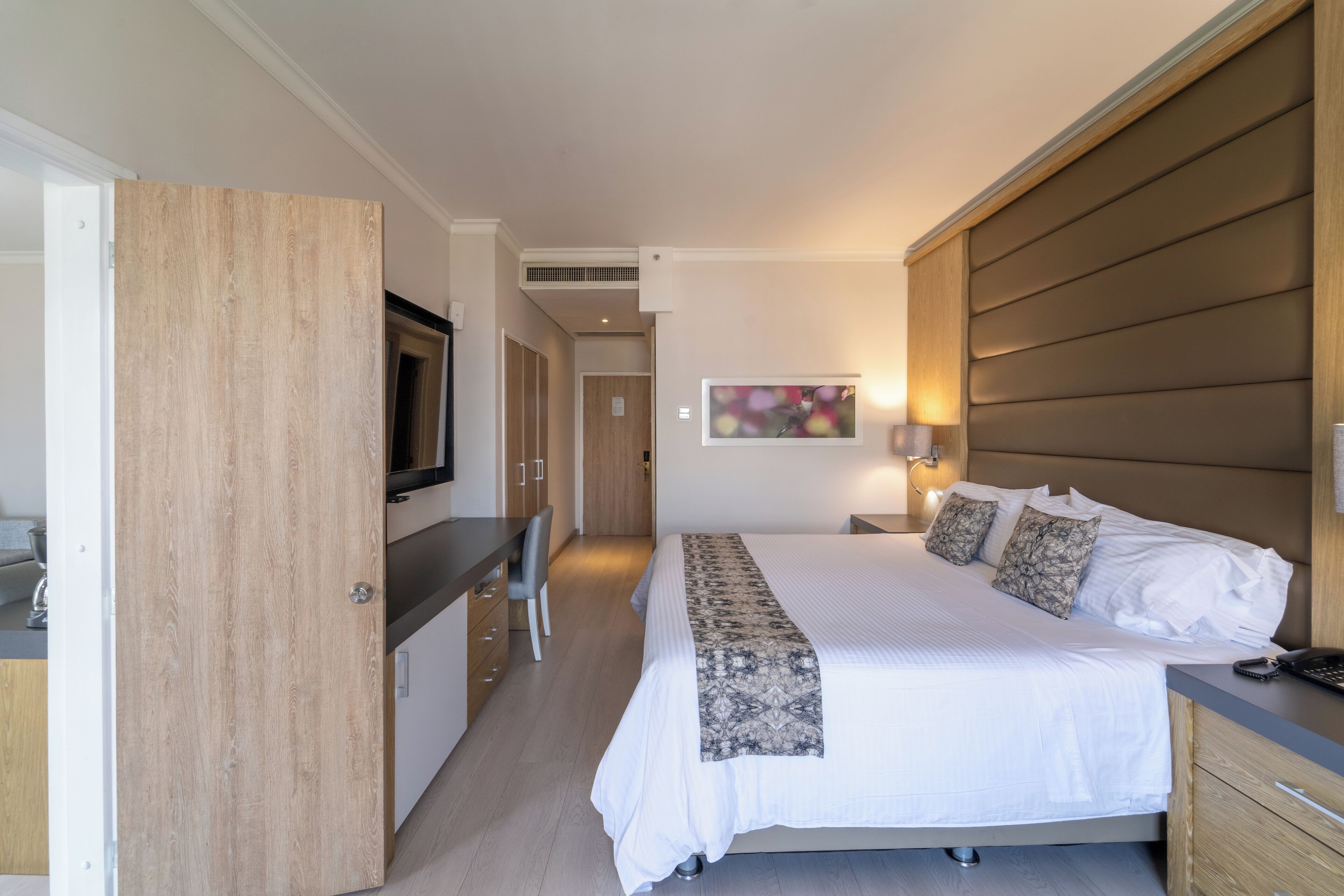 Une chambre d’hôtel avec un lit, une table de chevet, une télévision, un bureau, une chaise et un tableau au mur.