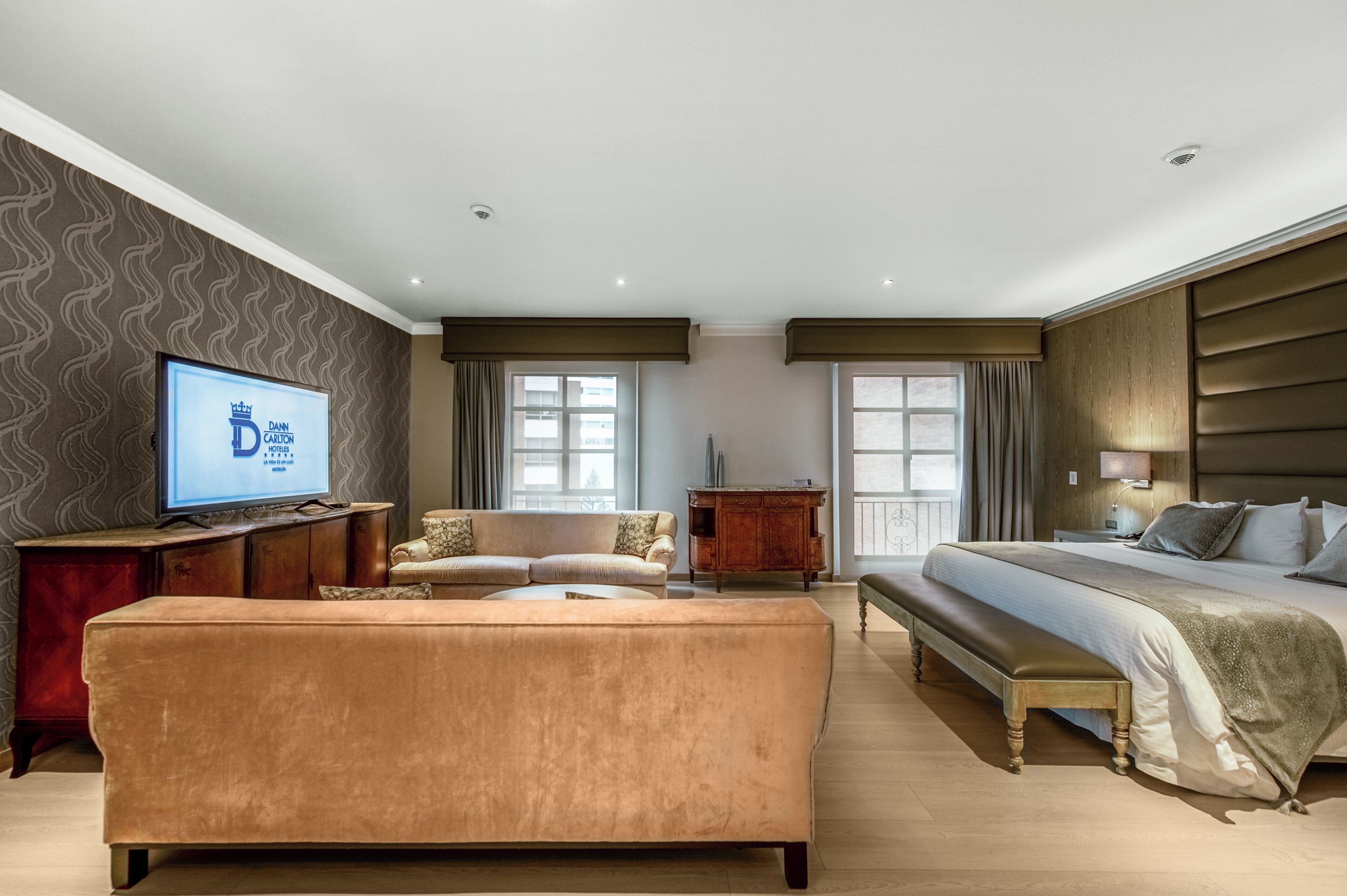 A hotel room with a large bed, a sofa, a TV, and a wooden cabinet.