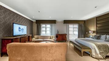 A hotel room with a large bed, a sofa, a TV, and a wooden cabinet.