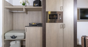 A compact kitchenette with a built-in microwave, a small countertop, and a shelf with a bag and flowers.