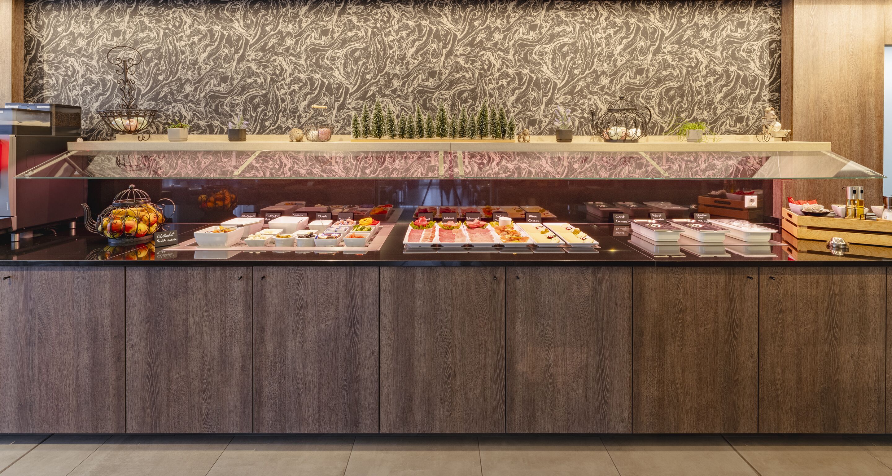 Mostrador de buffet con diferentes alimentos y una pared decorativa con diseño de mármol.