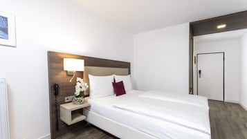 A hotel room with a large bed, a bedside table with a lamp, a vase with flowers, and a door.