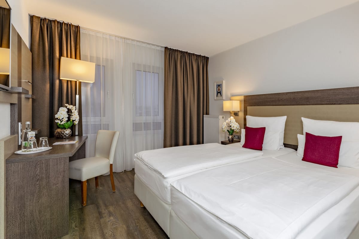 Habitación de hotel con una cama grande, un escritorio con silla y dos mesitas de noche con lámparas.