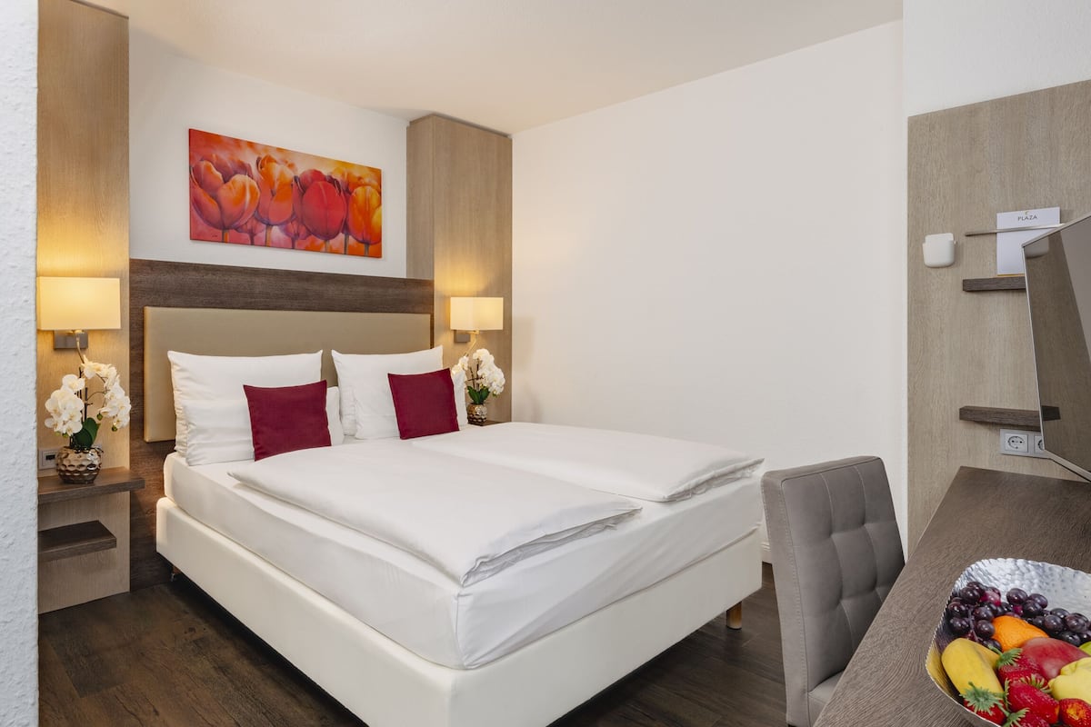 Una habitación de hotel con una cama grande, dos mesitas de noche con lámparas, un televisor montado en la pared y un frutero en la mesita auxiliar.