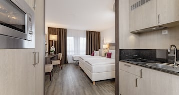 Habitación de hotel con kitchenette, cama, escritorio y silla.