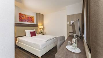 Ein Hotelzimmer mit Bett, Nachttisch mit Flasche und Glas, Spiegel und einem Gemälde an der Wand.
