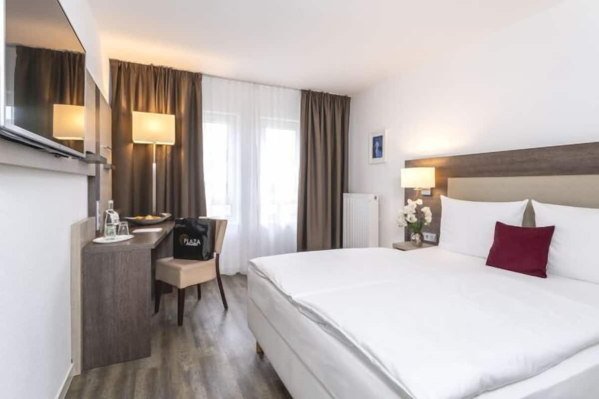 Habitación de hotel con cama, escritorio, silla, baño y ventana con cortinas.
