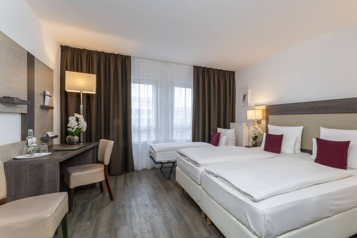 Una habitación de hotel con una cama grande, un escritorio, una silla y una ventana con cortinas.