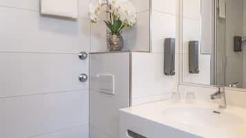 A modern bathroom with a white sink, a mirror, a vase with white flowers, and a soap dispenser.