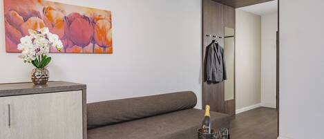 A modern living room with a grey sofa, a decorative vase with white flowers, a bottle of champagne, and two glasses on a small round table.