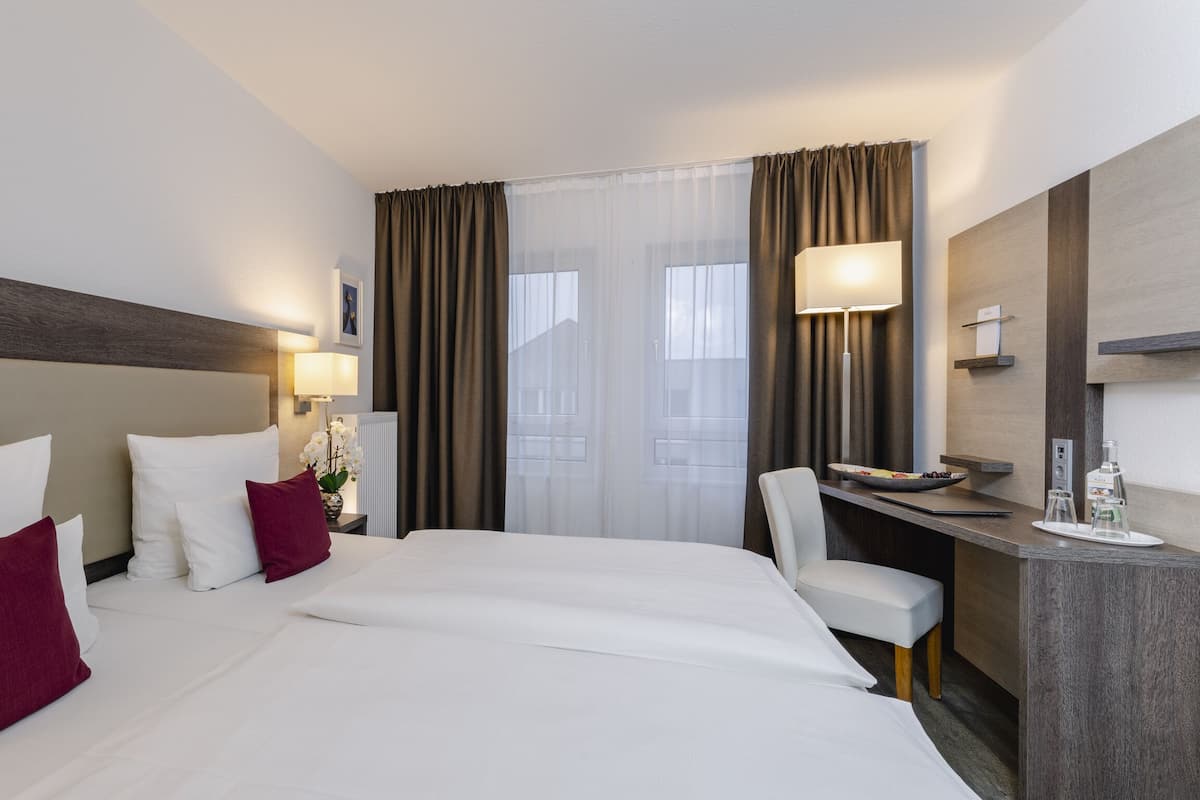 Habitación de hotel con una cama grande, un escritorio, una silla y una ventana con cortinas.
