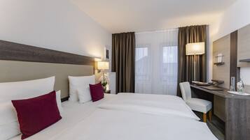 Habitación de hotel con una cama grande, un escritorio, una silla y una ventana con cortinas.