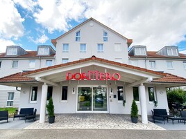 Entrada de un hotel con un cartel que dice 'DORMERO' y una zona de acceso cubierta con sillas y plantas en macetas.