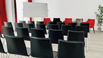 A conference room with rows of black chairs, a whiteboard, and red and grey chairs in the background.