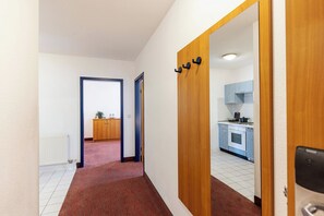 Un couloir avec un tapis rouge, une porte en bois ornée d’un miroir, et une vue sur une cuisine aux armoires bleues.