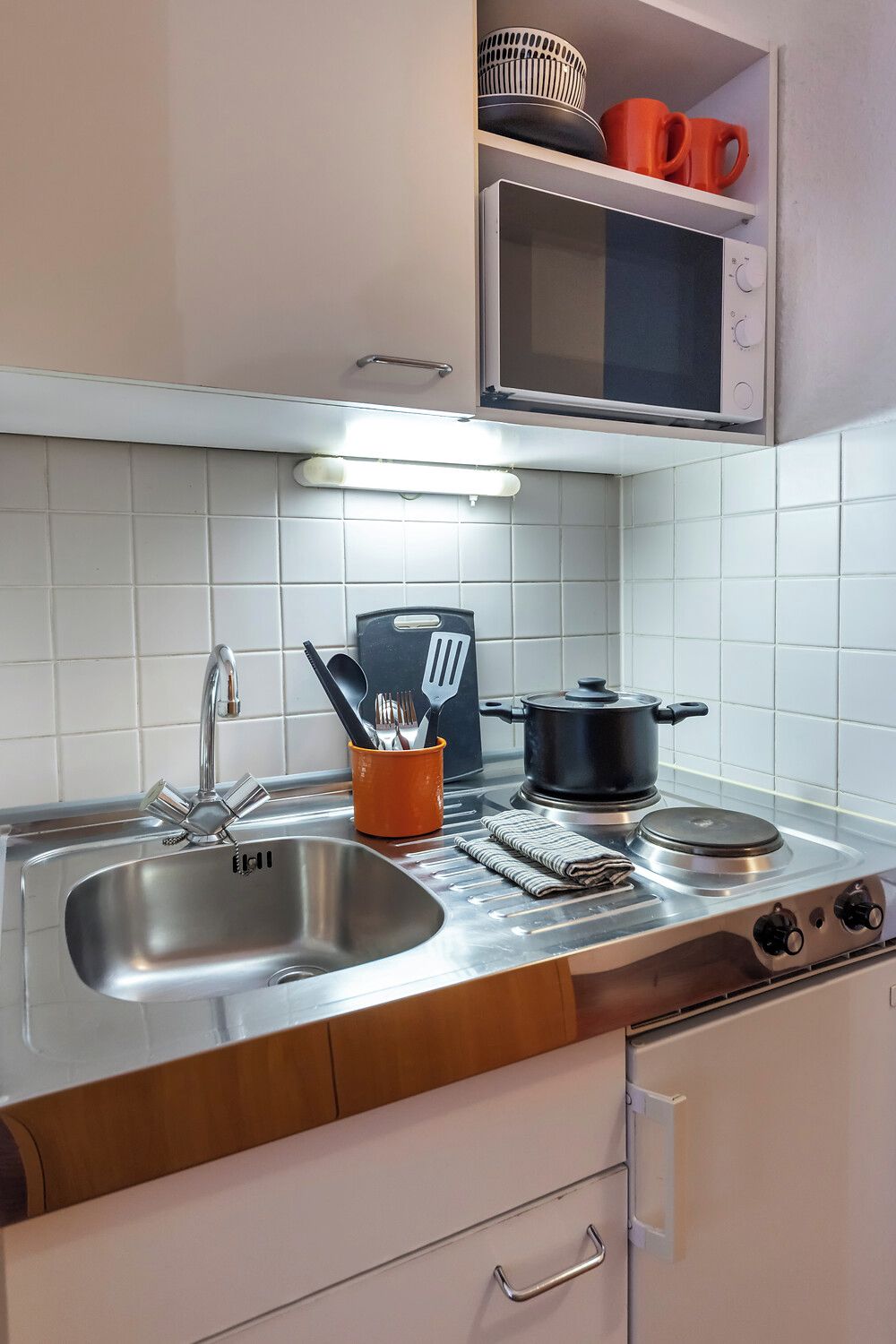 Una cocina con un lavamanos de acero inoxidable, una estufa, un microondas y una encimera con utensilios de cocina.