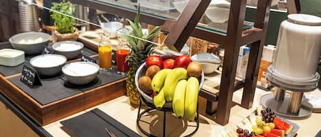 A breakfast buffet with various fruits, a coffee machine, and a juice dispenser.